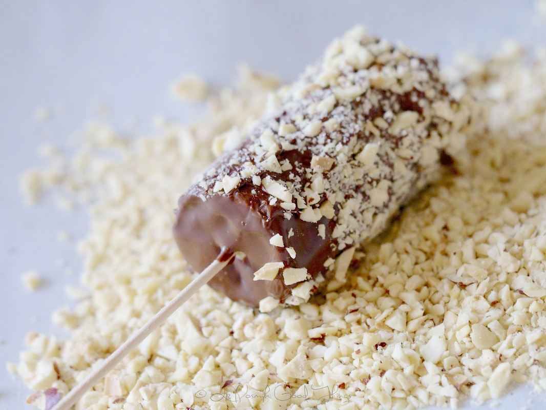 Dip the banana pops into the tempered chocolate and then the hazelnuts 