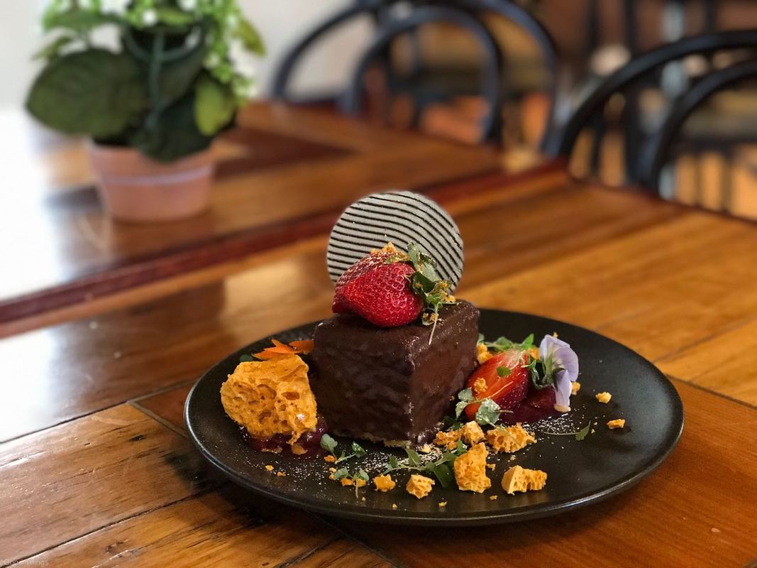 Layered chocolate mousse sponge cake with rhubarb and pear compote, a scattering of honeycomb, a chocolate disc, fresh strawberries and lemon balm micro herbs